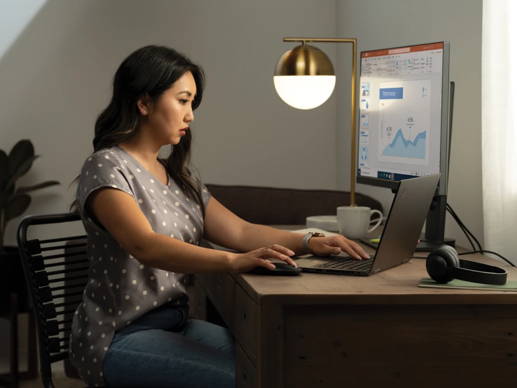 A woman working at her home office on a Lenovo ThinkPad Yoga connected to an external monitor displaying a PowerPoint file. Remote Working collection. Keywords: remote work, remote working, work from home, working at home, home office