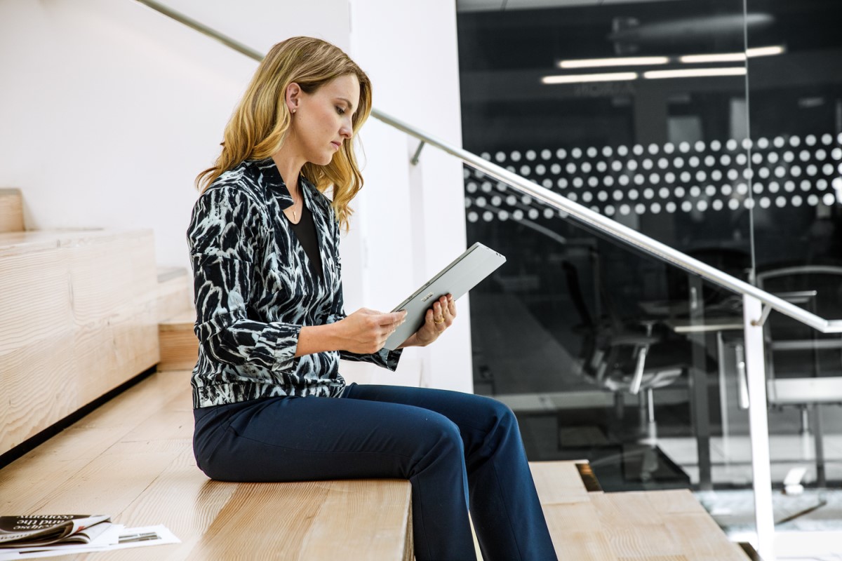 Woman sitting on steps in open office building. She is using a tablet.
