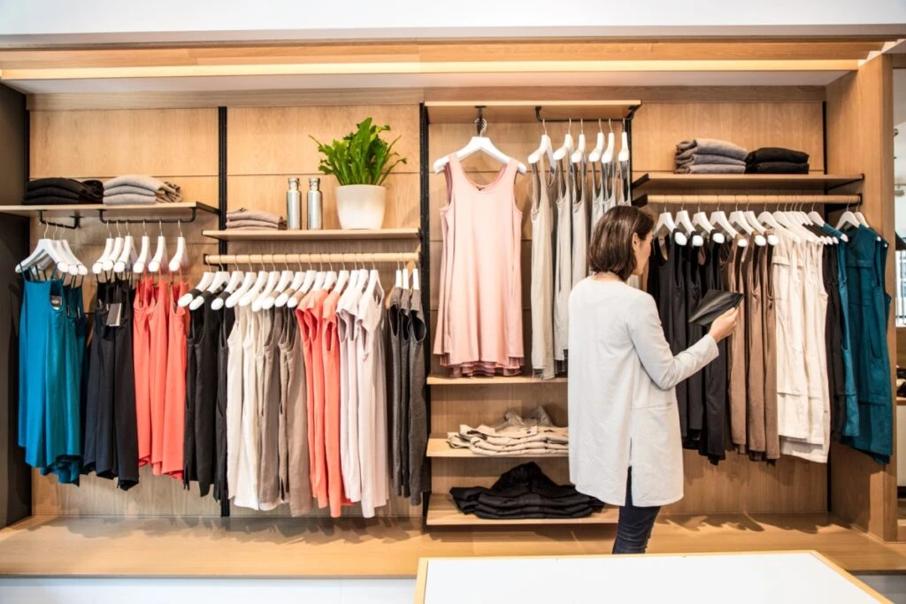 Female store employee using tablet in front of retail clothing display.