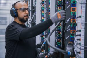 Male datacenter employee plugs cable in hot aisle power distribution unit.