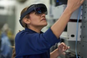 Field engineer inspects electrical substation server room on a wind farm using remote assist with HoloLens2. Keywords: Dynamics 365; operations; woman; green energy; remote training