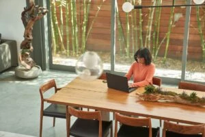 Overhead view of business decision maker (BDM) working from home on a laptop. Keywords: Security; Dynamics 365; woman; device; secure; dining room table; conference room table; hybrid work; manager; focused work; end user scenario; seller; CISO; chief information security officer