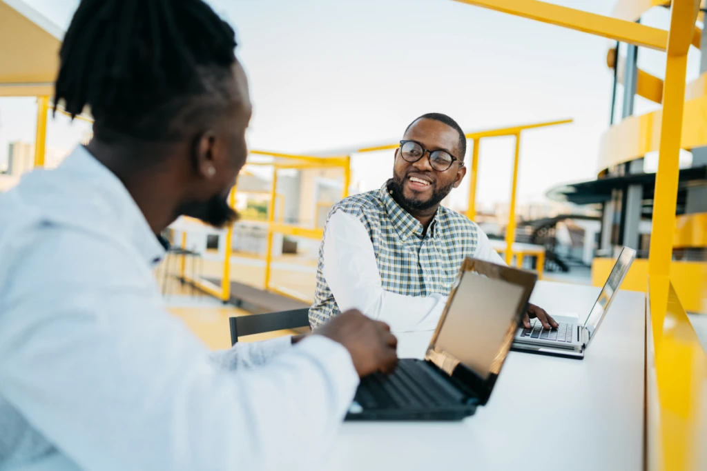 Two men work together on laptops in outdoor workspace