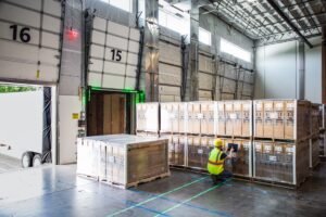 Worker in hardhat and reflective vest using tablet in warehouse loading dock.