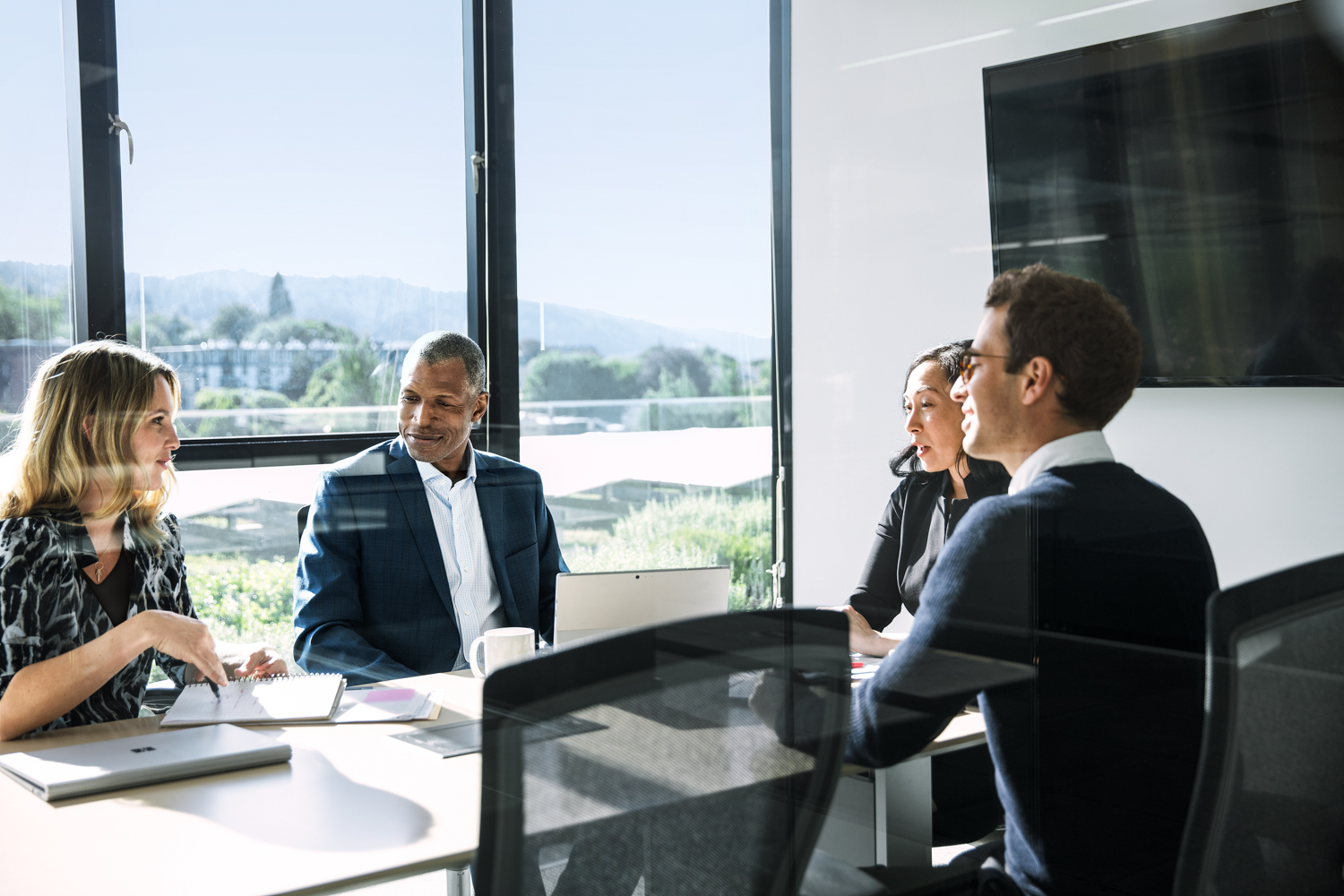 Photo of four people seated around a table in a windowed conference room.