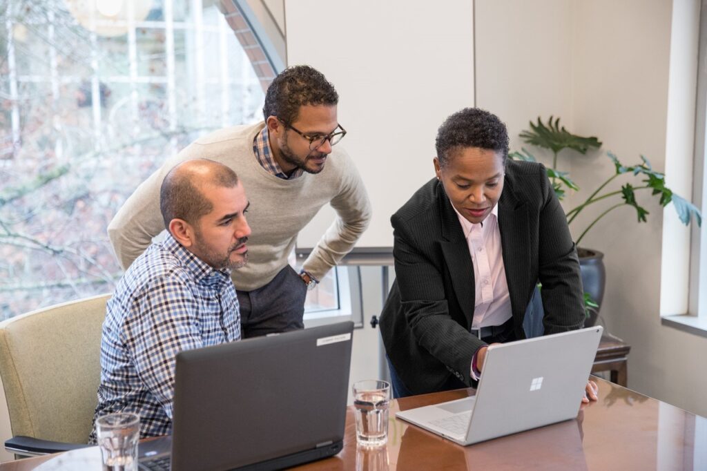 Three people at a conference table, looking at a laptop.