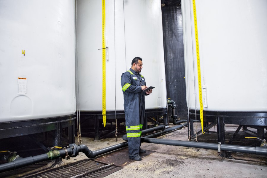 Male worker wearing utility suit using tablet. Industrial vats visible in background.