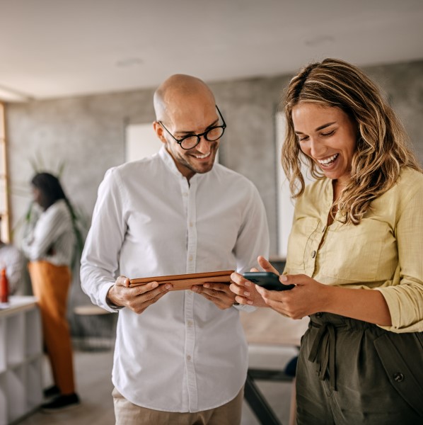 Two employees standing together, one holding a tablet and the other holding a phone that they're both looking at