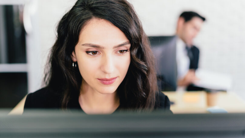 Close-up portrait of a Caucasian businesswoman typing and looking on a computer screen with intention at her desk. Concern and fix problems in a corporate office.