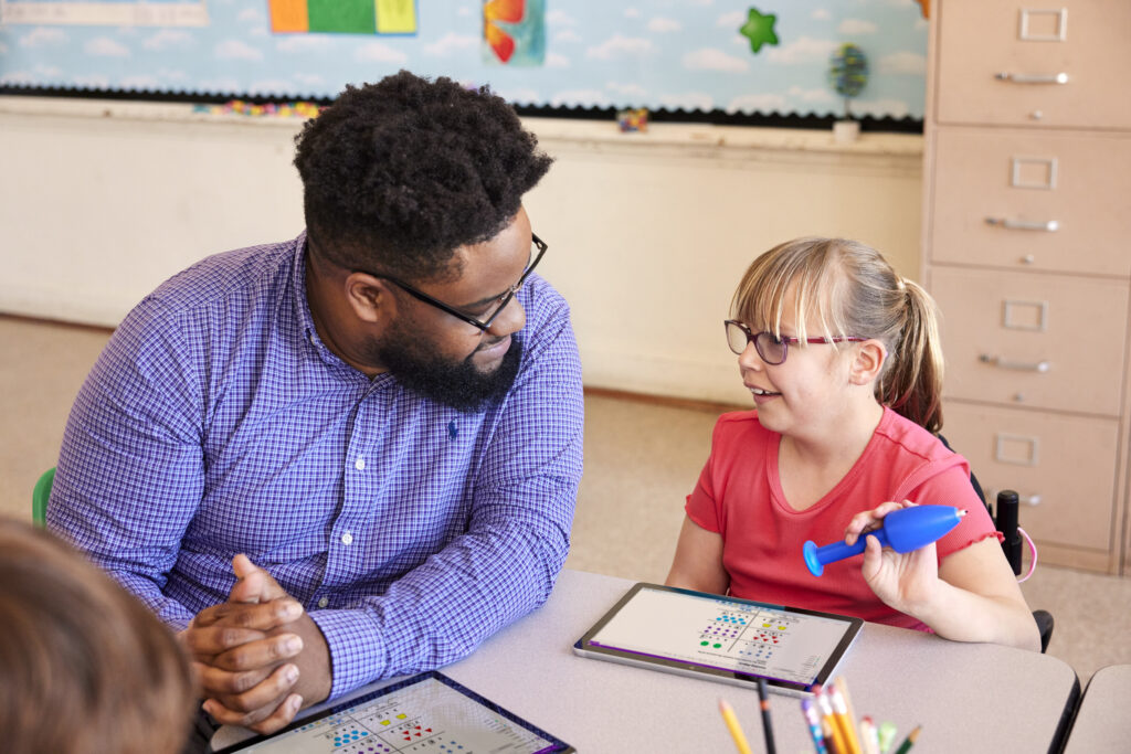 A teacher working with a student on an assignment on a tablet in a classroom setting.