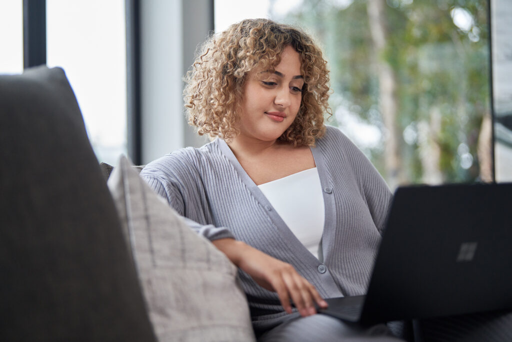 An educator sits on a sofa while looking at a laptop screen.