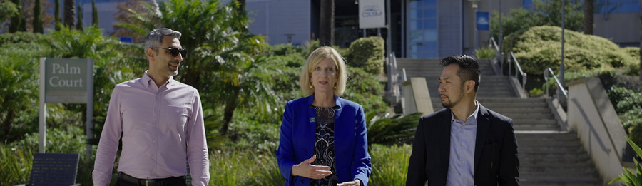 Three higher education leaders walk together outside on a college campus.