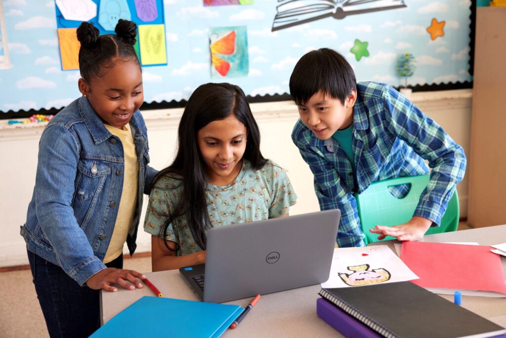 Classroom scene showing three smiling students collaborating on a laptop.