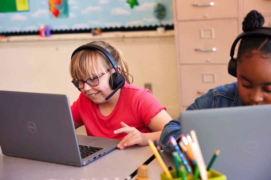 Two students in a classroom using laptops with headsets.