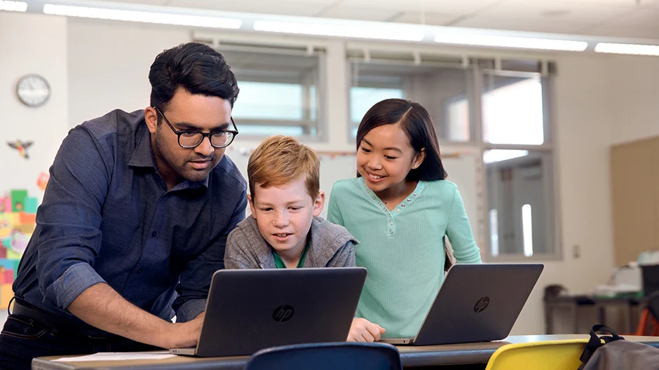 A teacher helping two students working on laptops. 