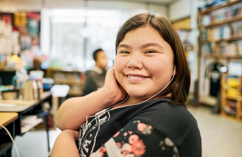 Decorative. A student sits at a desk in a school classroom and faces the camera.