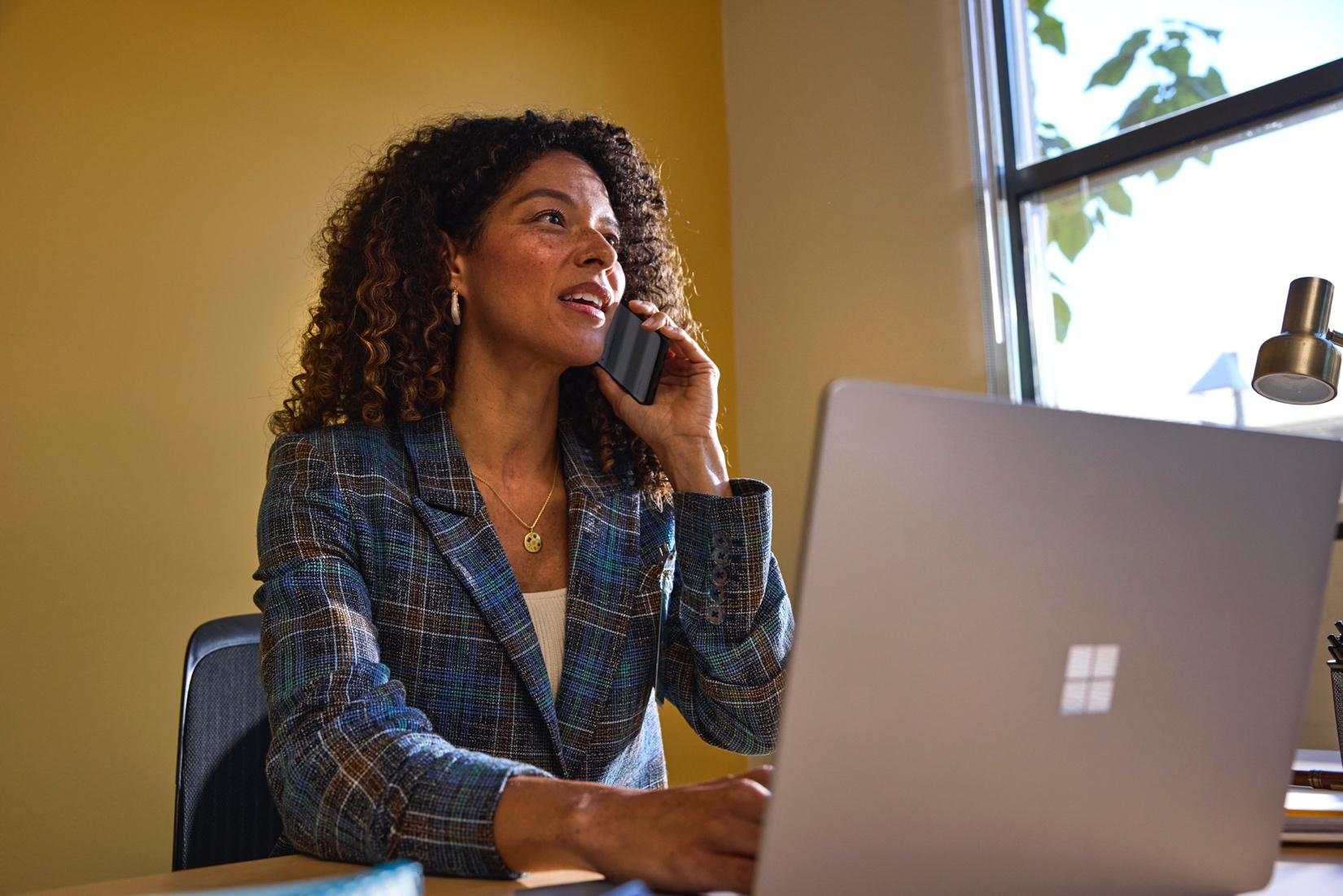 An education leader sits at a desk using a phone and laptop.
