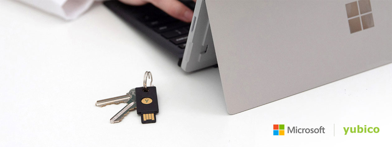 Hands typing on a Microsoft table next to a YubiKey