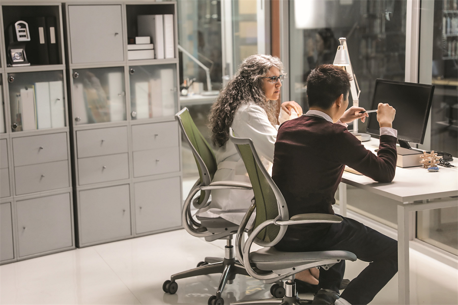 A doctor and a patient sitting at a desk in front of a computer monitor