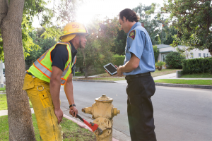 Firefighters looking a a tablet computer next to a hydrant.