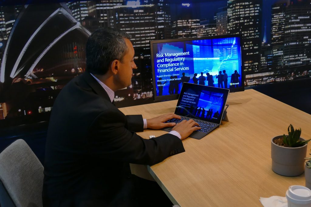 Person sitting at desk with a Surface laptop projecting a Financial Services presentation onto a monitor