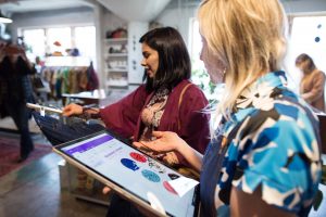 Retail store employee holding laptop helping customer with a pair of jeans