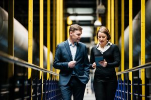 Two business persons walking through a factory hallway