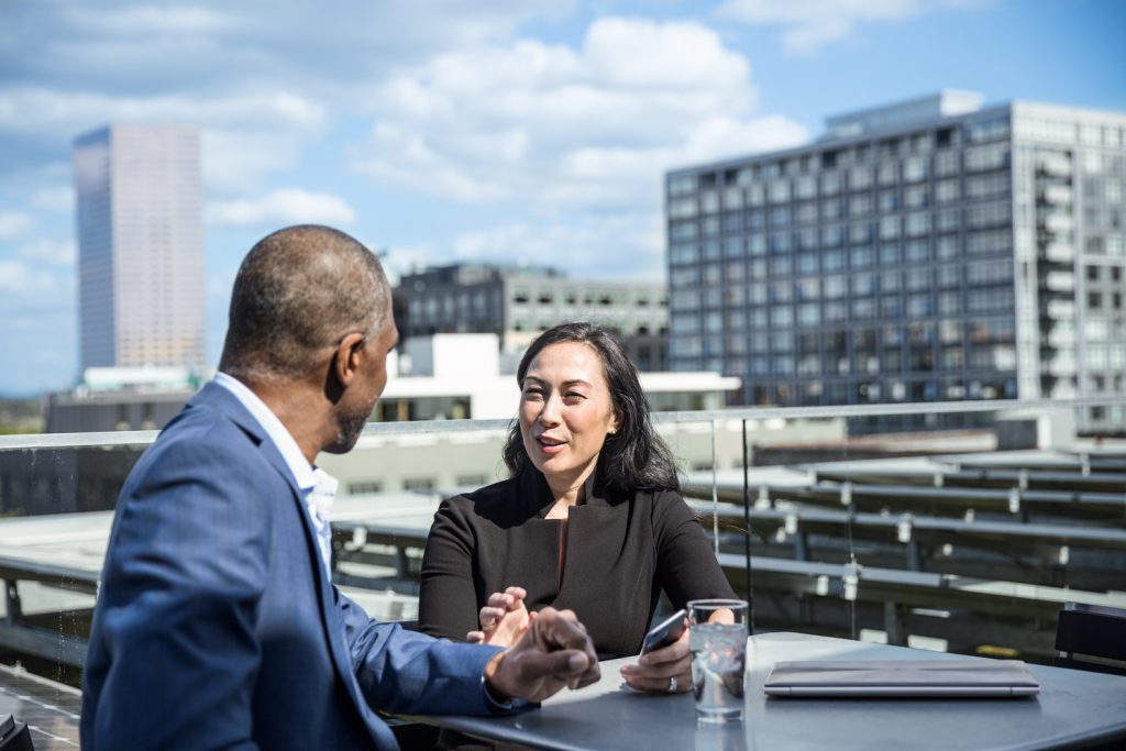 two people talking outdoors with a cityscape in the background