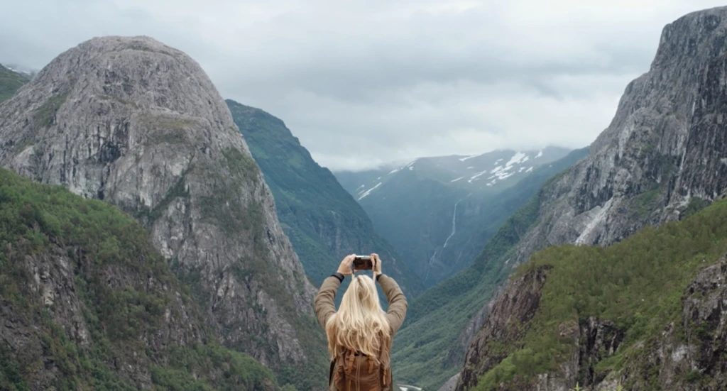 A person standing and taking a photo in front of a mountain