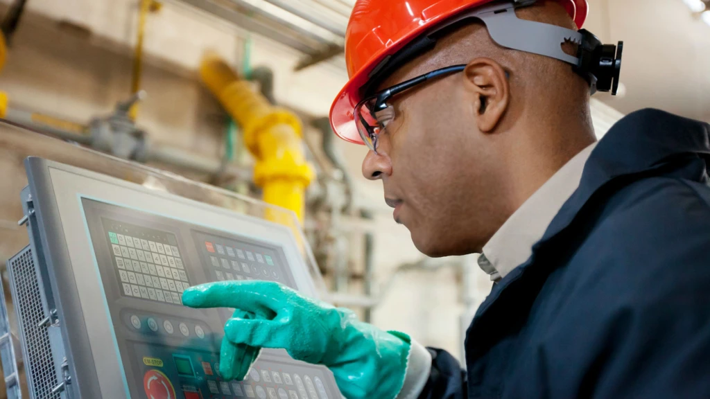 man in a hard hat looking at a computer screen in a factory