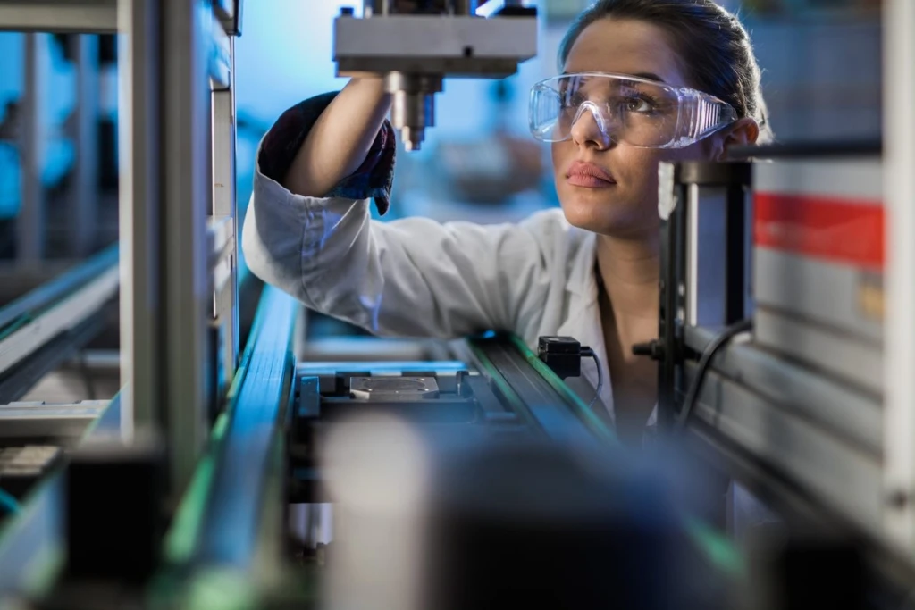 woman looking at a piece of machinery wearing safely goggles