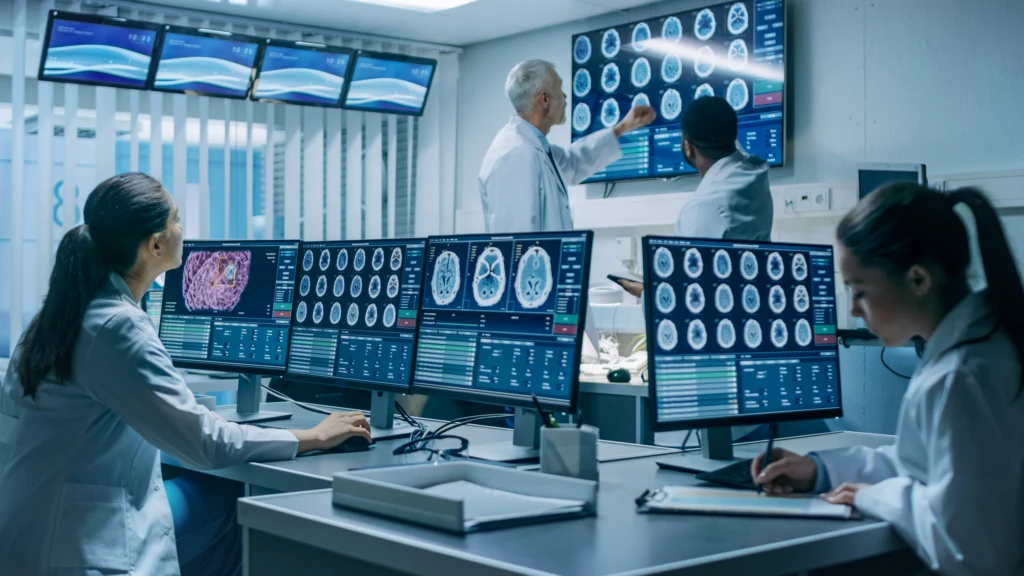 Team of Professional Scientists Work in the Brain Research Laboratory. Neurologists / Neuroscientists Surrounded by Monitors Showing CT, MRI Scans Having Discussions and Working on Personal Computers.