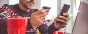 1. A man in a holiday sweater holding a credit card and using his smartphone.