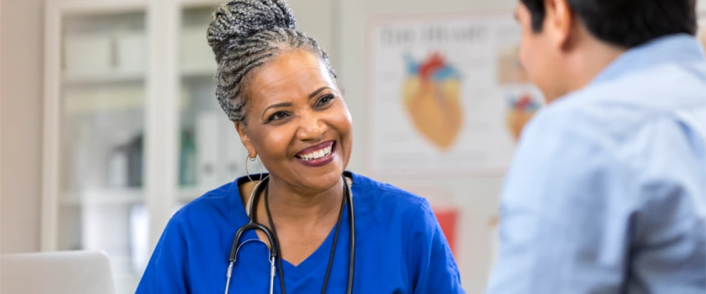 A person in scrubs smiling looking at another person.