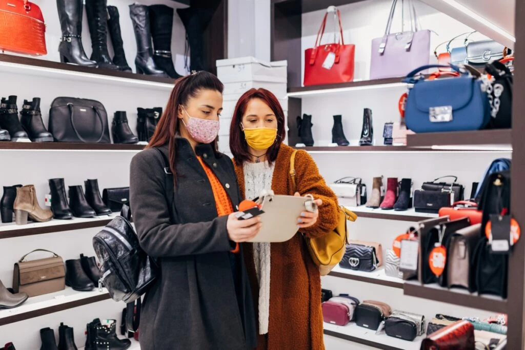 Two females in retail store looking at a handbag with masks on