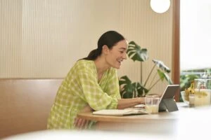 Woman sitting in kitchen working on 2-in-1 tablet in laptop mode.