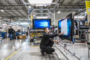 Millenial man squatting to use large touchscreen monitor (screen shown) in test factory