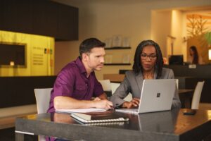 Two professionals in a bank setting looking at financial matters on a laptop screen together