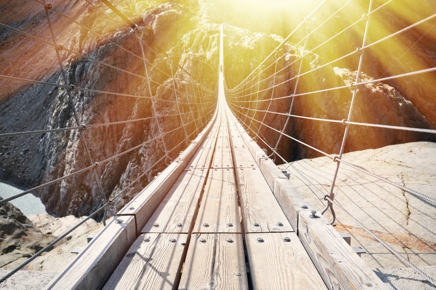 A sunlit suspension bridge crossing a broad, glacial canyon