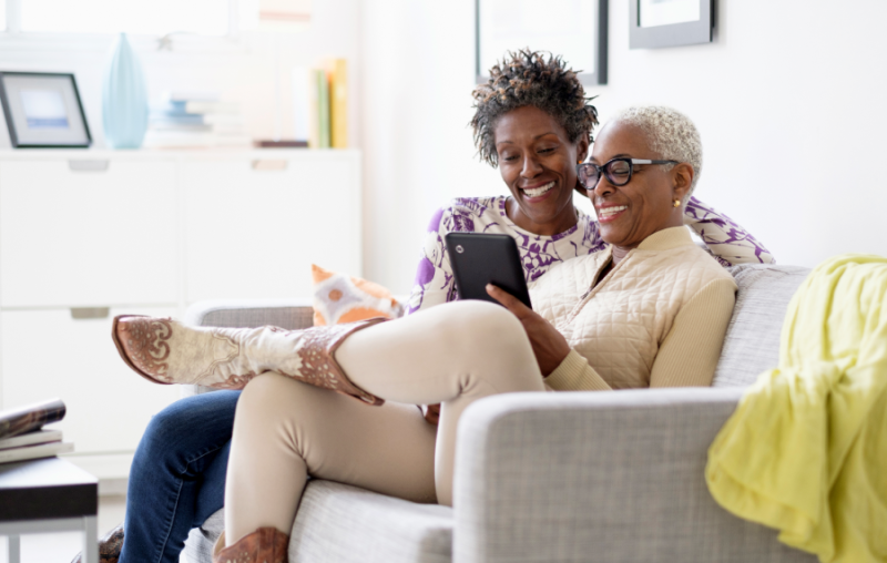 Two mature African American women sitting on a couch interacting with an app on a tablet.