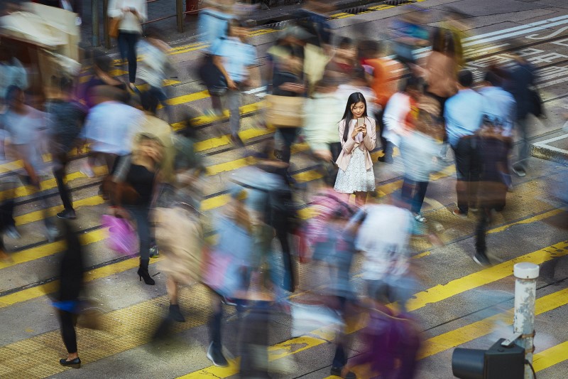 A person using their mobile phone in a crowd of people that are blurred.