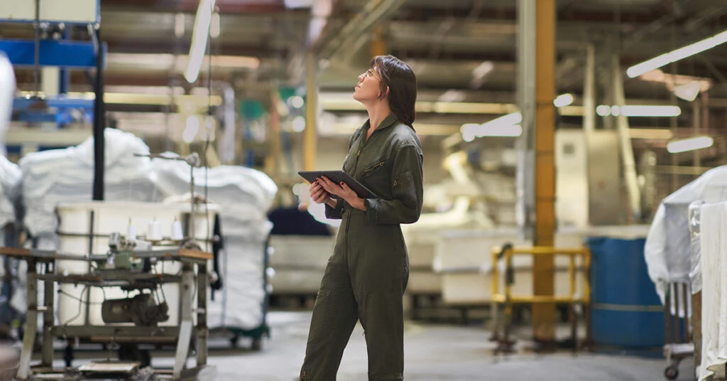 繊維工場内でタブレットを手に生産ラインを見上げている女性従業員