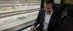 Ein Geschäftsmann sitzt mit Headset im Zug und arbeitet