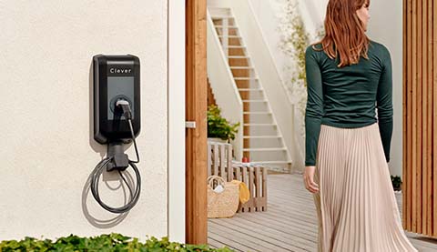An electric charging station and a woman who is entering a house.