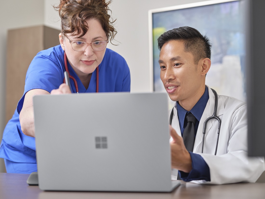 Eine Krankenschwester und ein Arzt blicken gemeinsam auf den Bildschirm eines Surface Laptops.