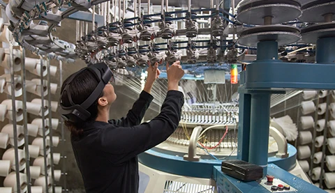 Frau trägt eine Hololens und blickt auf eine Maschine der Textilindustrie