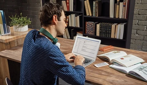 Man sitzt an einem Schreibtisch mit seinem Laptop. 