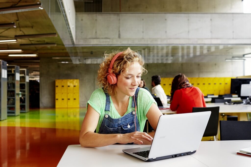 Eine blonde Studentin sitzt an einem Tisch und arbeitet mit einem Acer Device