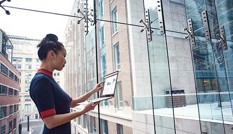 Frau mit Laptop vor einer großen Glasfront.