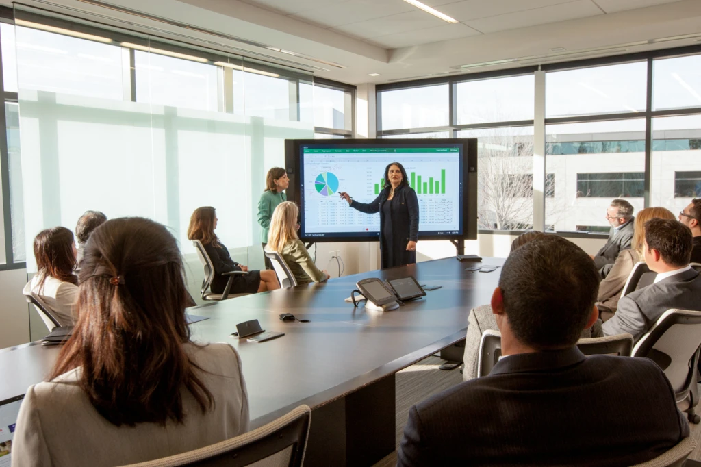 CEO leading a financial meeting using the Surface Hub. Business attire.